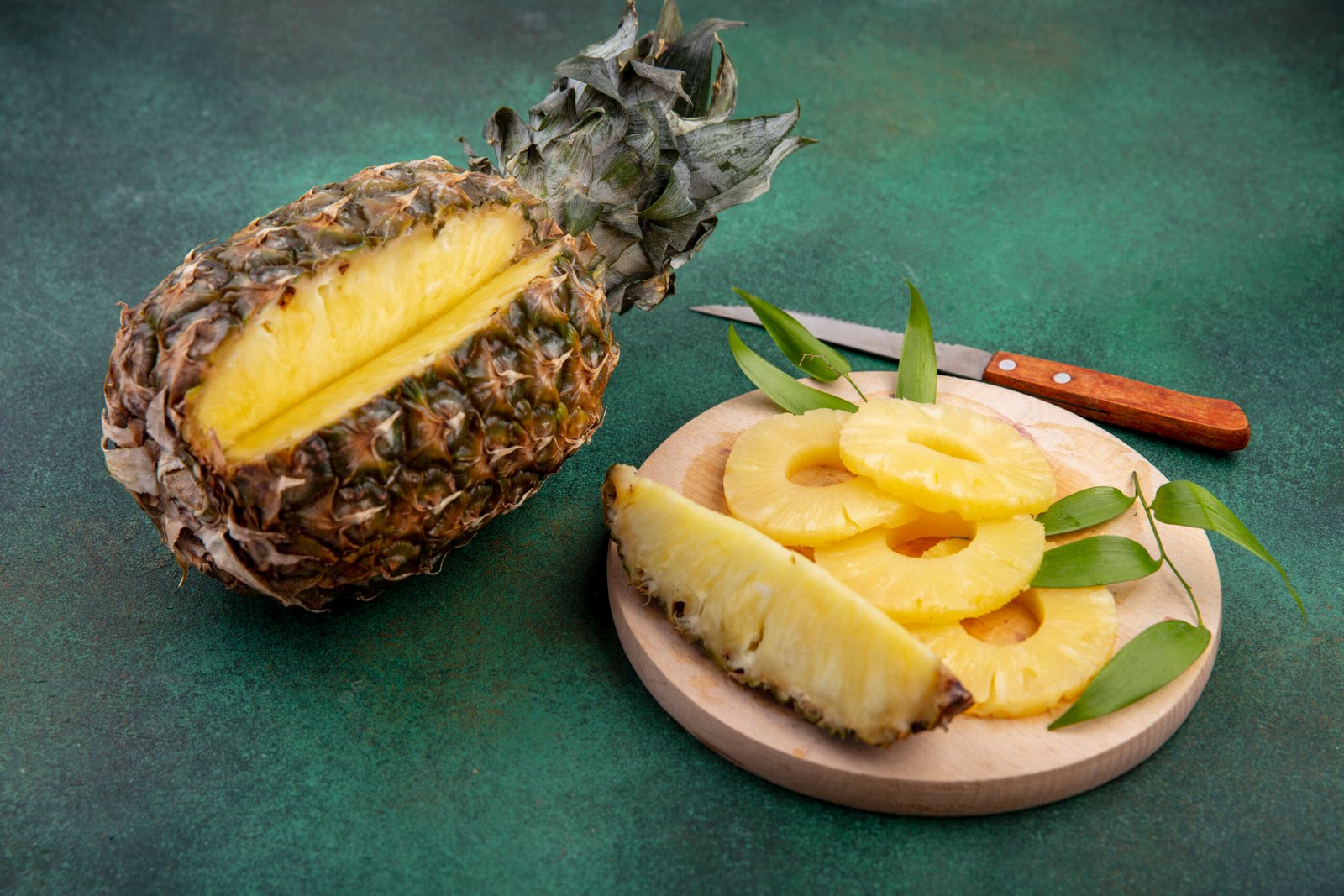 front-view-pineapple-with-one-piece-cut-out-from-whole-fruit-pineapple-slices-cutting-board-with-knife-green-surface-scaled.jpg